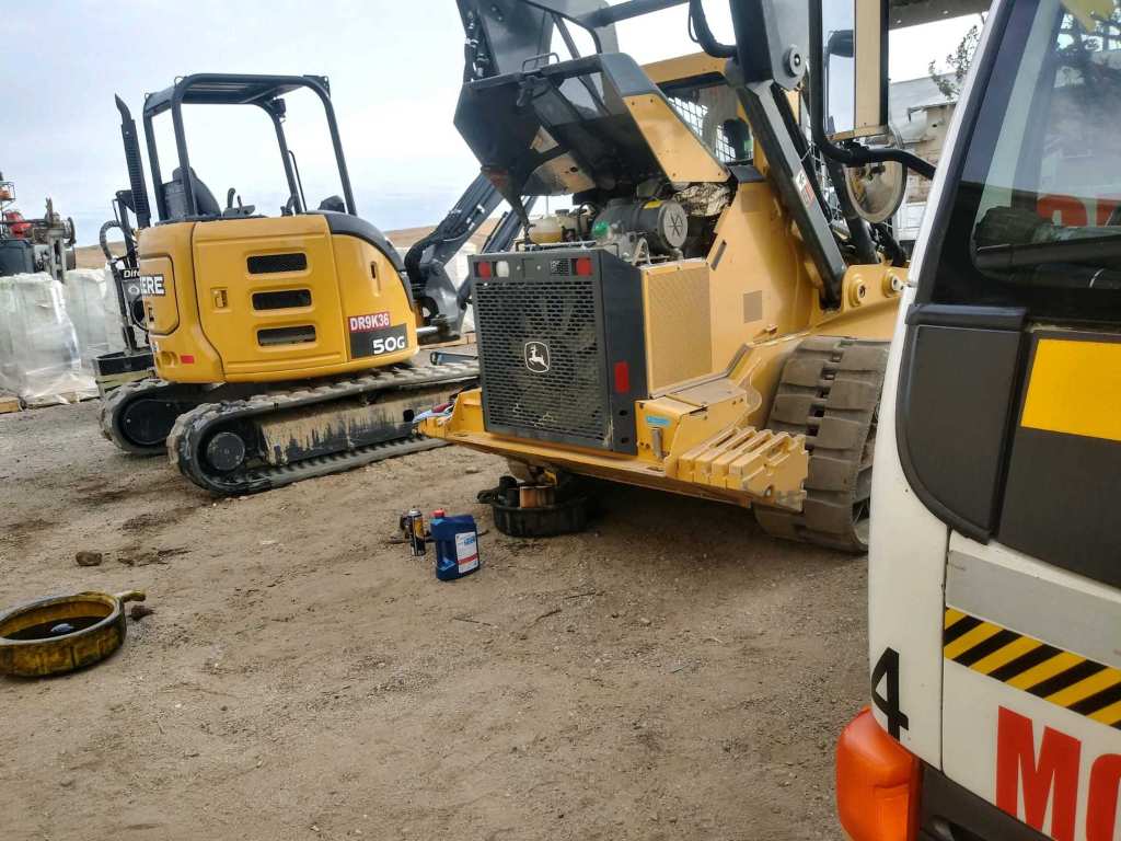 A yellow heavy machinery vehicle being serviced on a construction site, with tools and equipment visible on the ground.